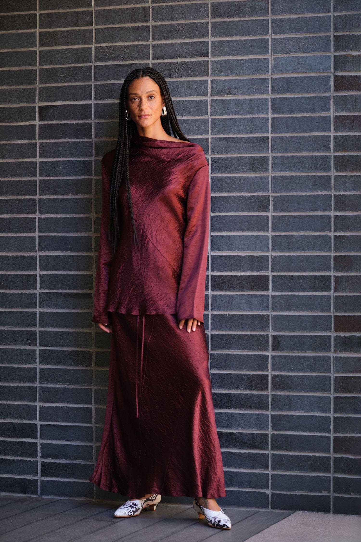 Woman wearing a perfect holiday outfit of Lauren Manoogian silk Luster Top and Skirt standing against a tiled wall.