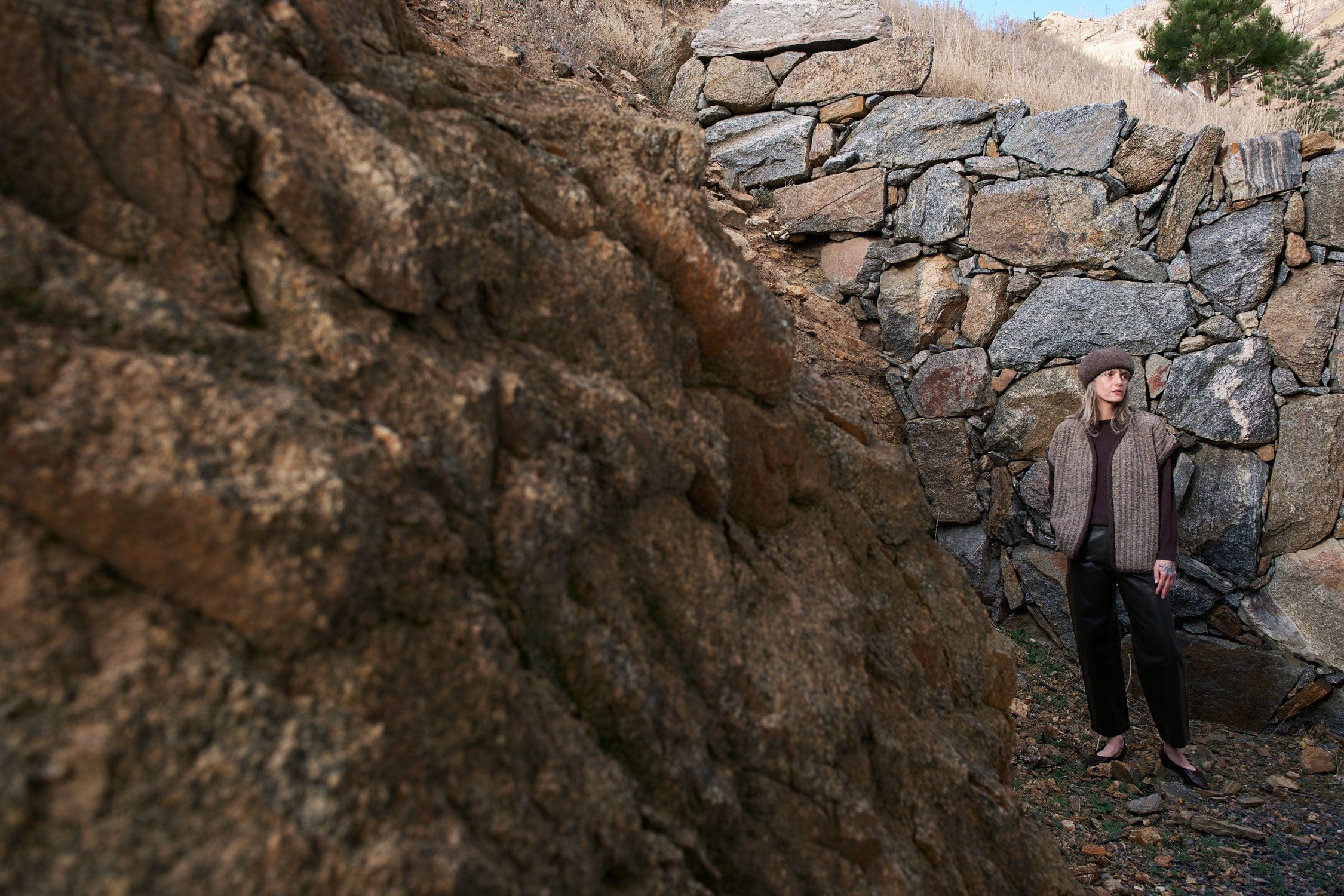 Person standing in front of a stone wall in a natural setting