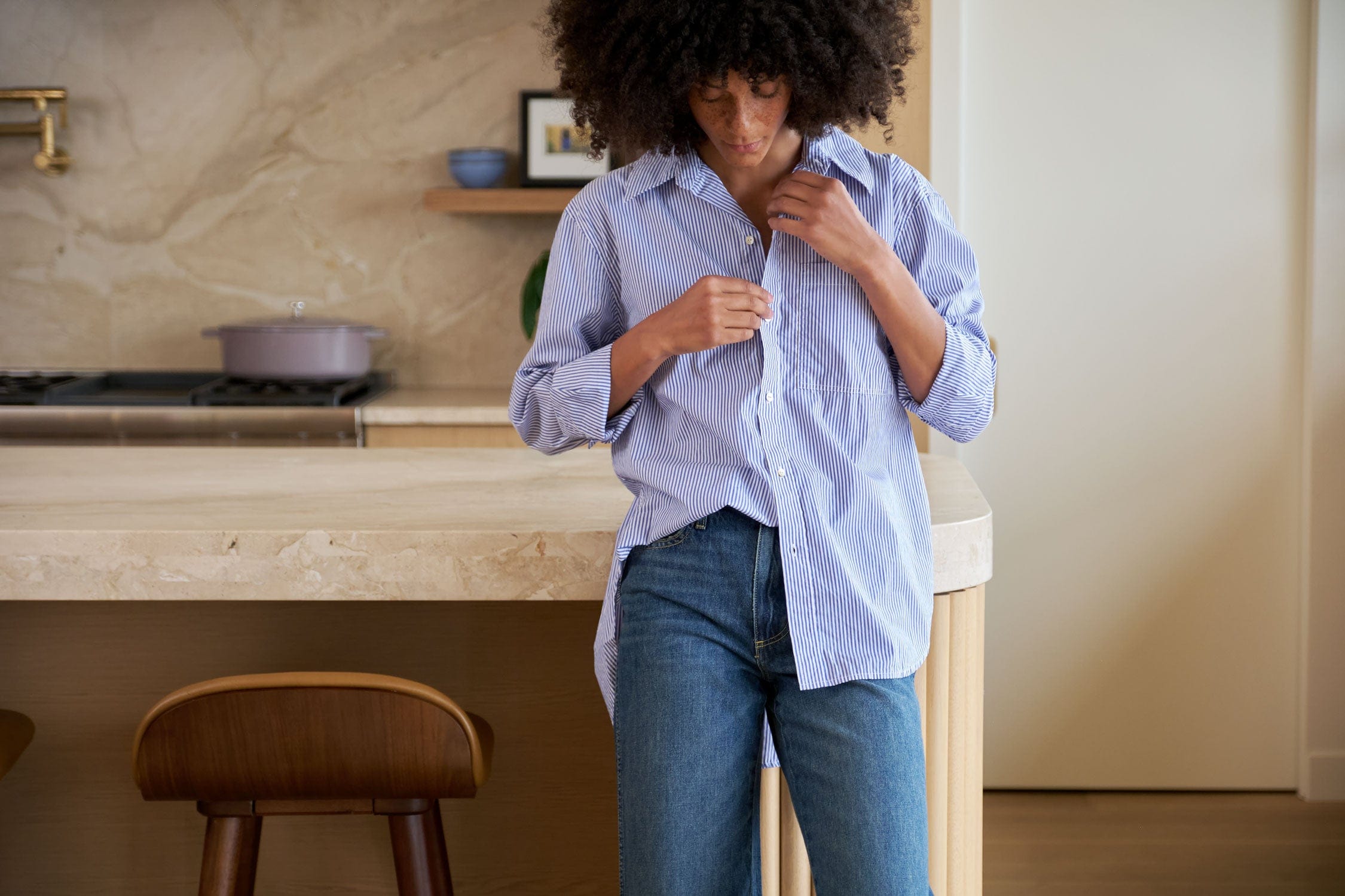 Person adjusting a blue shirt from AMO Denim in a kitchen