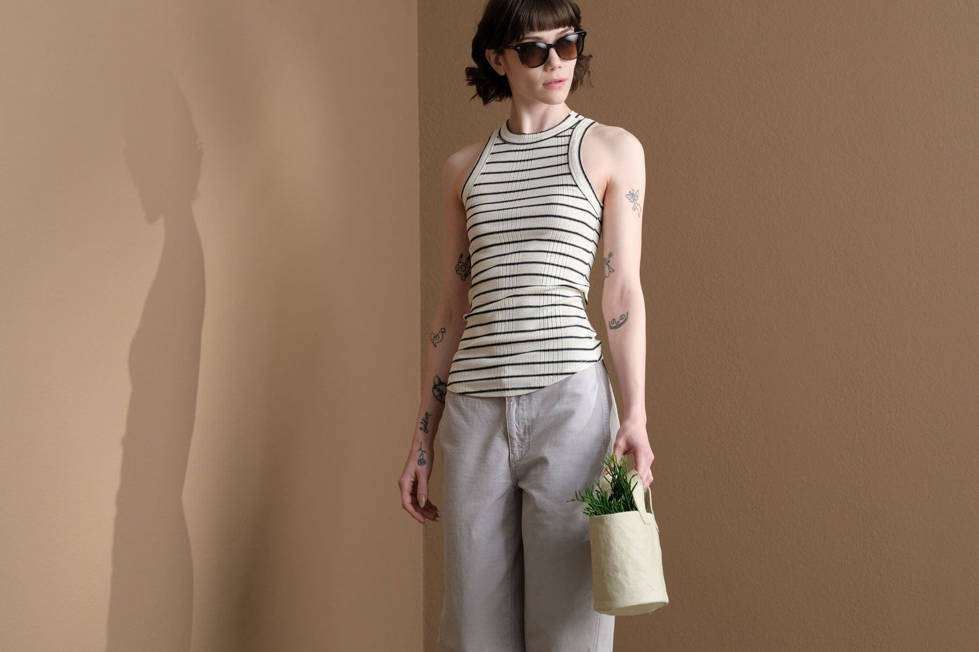 Person wearing a Amo Denim striped tank top and holding a small Uashmama bag against a beige background
