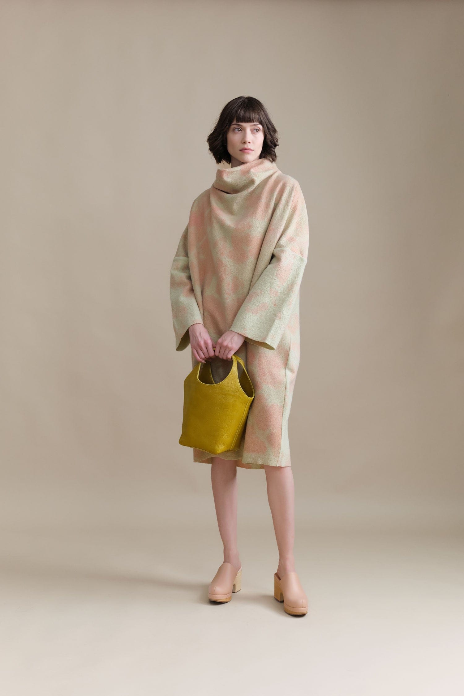 Woman wearing a pastel-colored dress from Anntian holding a yellow Lindquist bag against a beige background