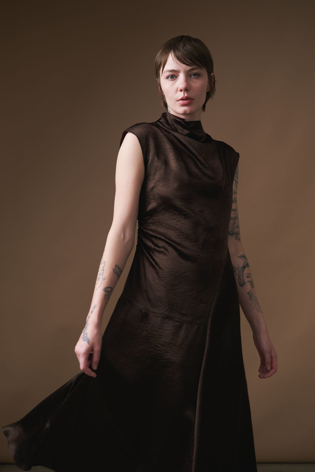 Woman wearing a dark brown dress by Atelier Delphine against a brown background