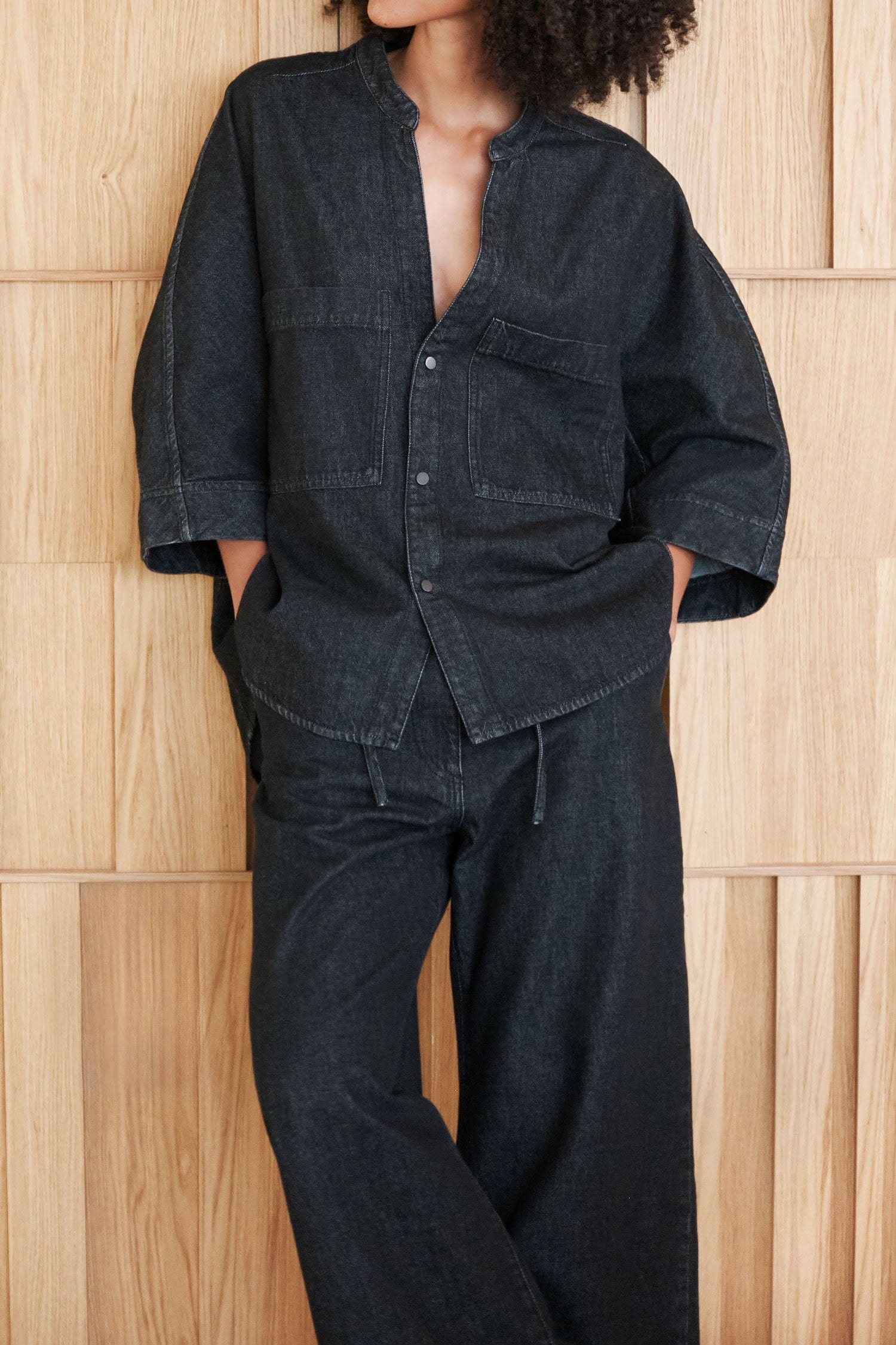 Person wearing a dark denim outfit  from Christian Wijnants against a wooden paneled wall