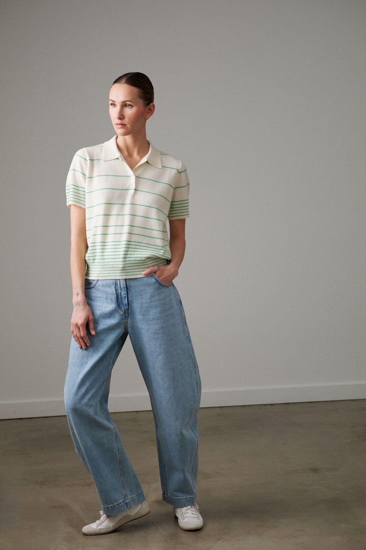 Woman wearing a Demylee cashmere striped polo shirt and Rachel Comey blue jeans against a plain background