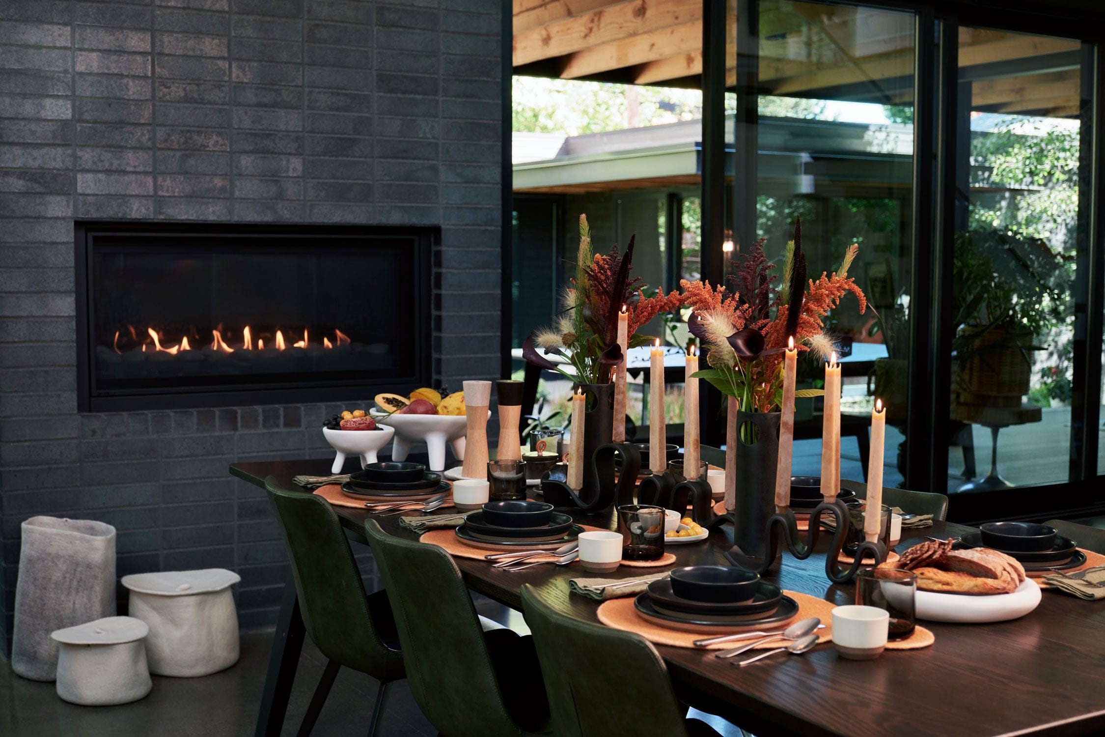 Dining room with a fireplace, table set for a holiday meal, and outdoor view through large windows.