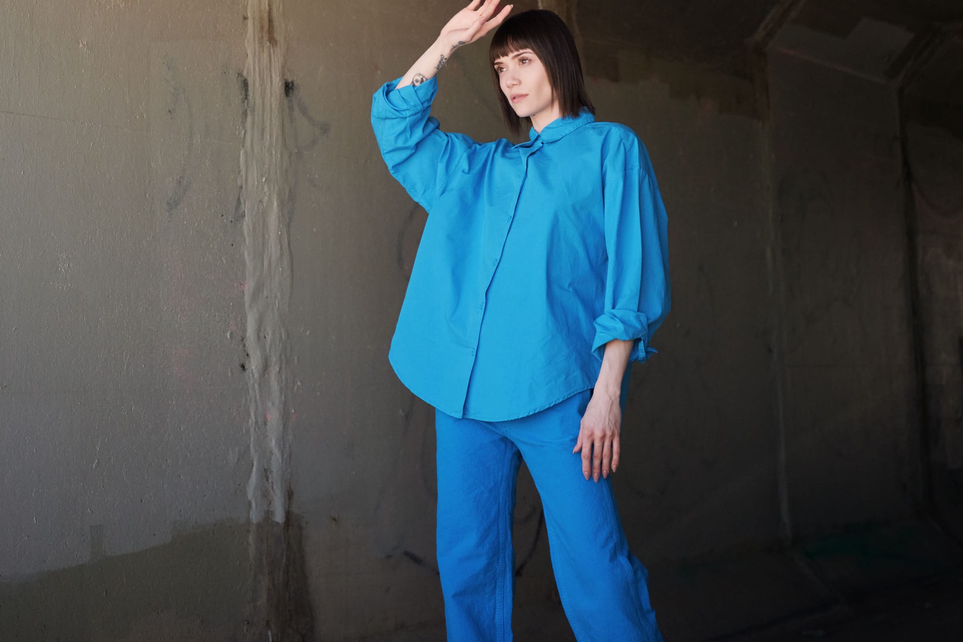 Person wearing a Jesse Kamm bright blue outfit against a dark textured wall