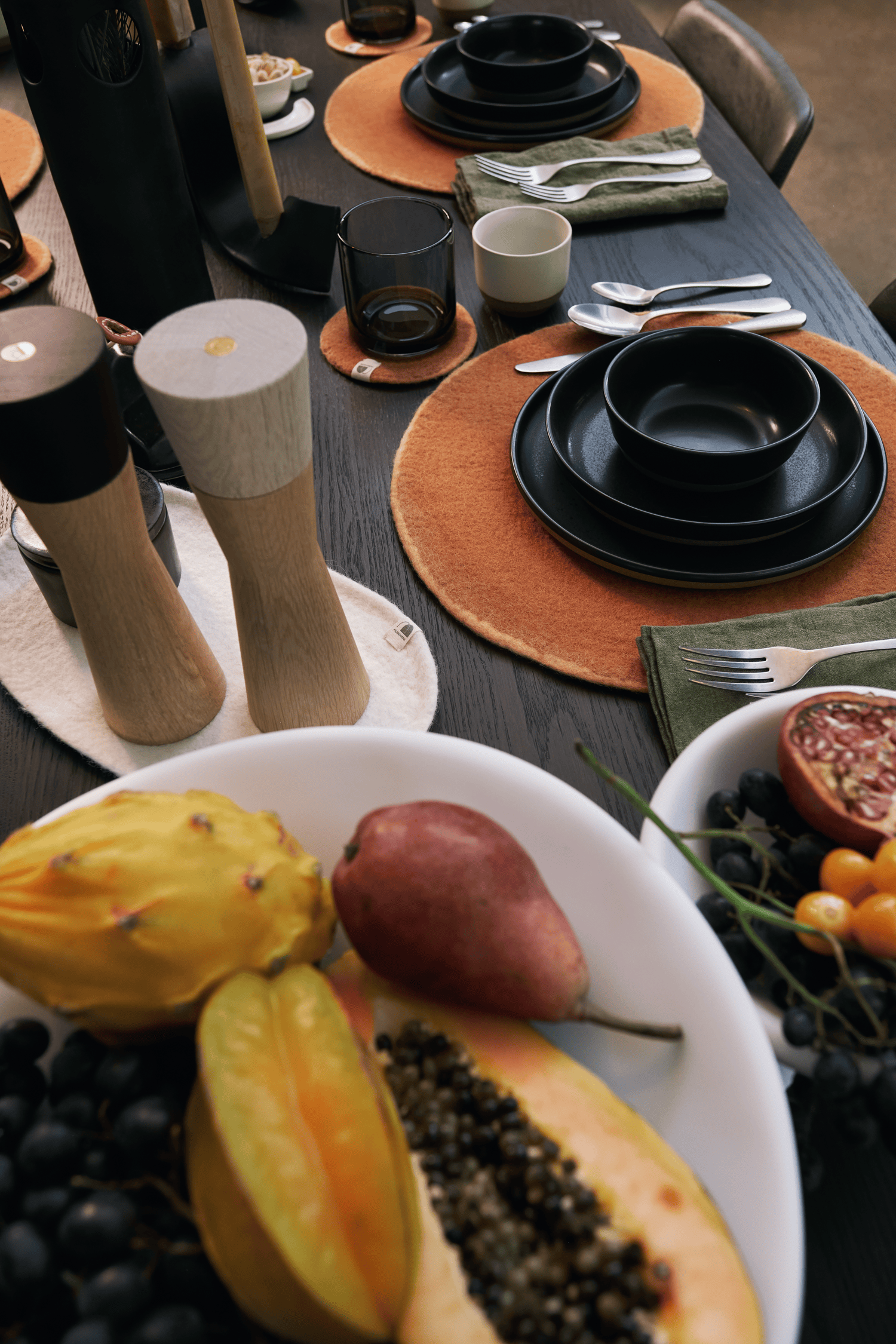 Holiday Dining table setting with black Kinto plates, muskhane felt, and fruit on a white tina frey plate.