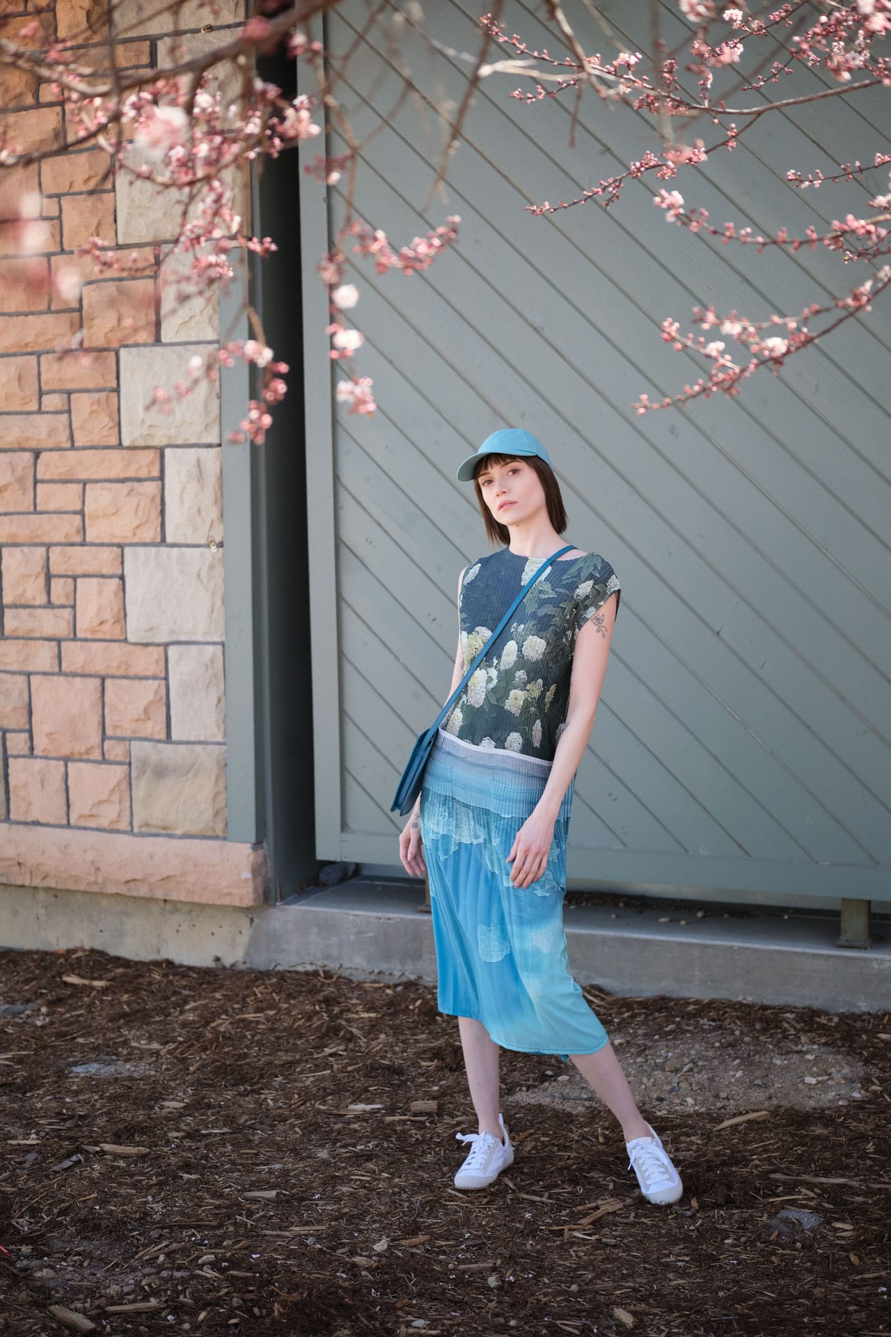 Woman wearing No. 6 Floral Print Dress with Lindquist bag standing in front of a building with cherry blossom branches.