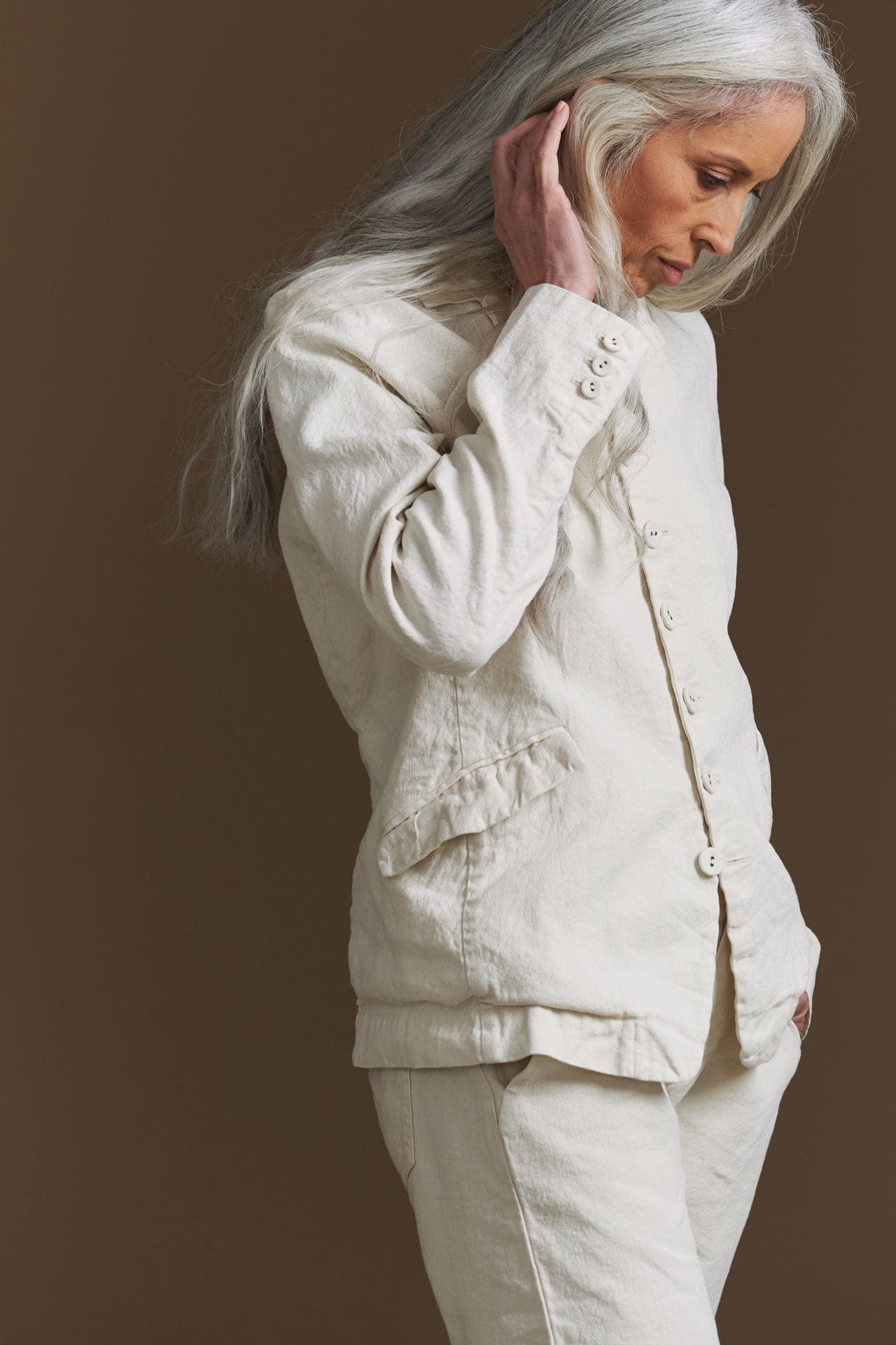 Woman wearing a white pas de calais jacket and pants against a brown background