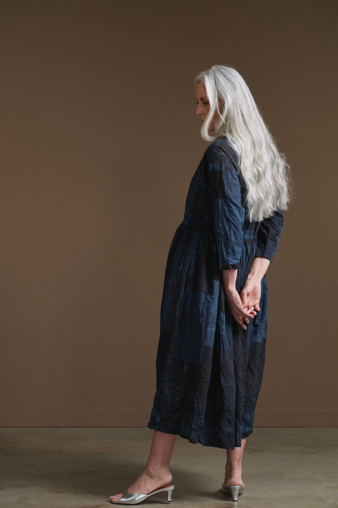 Woman wearing a blue Pas de Calais dress against a brown background