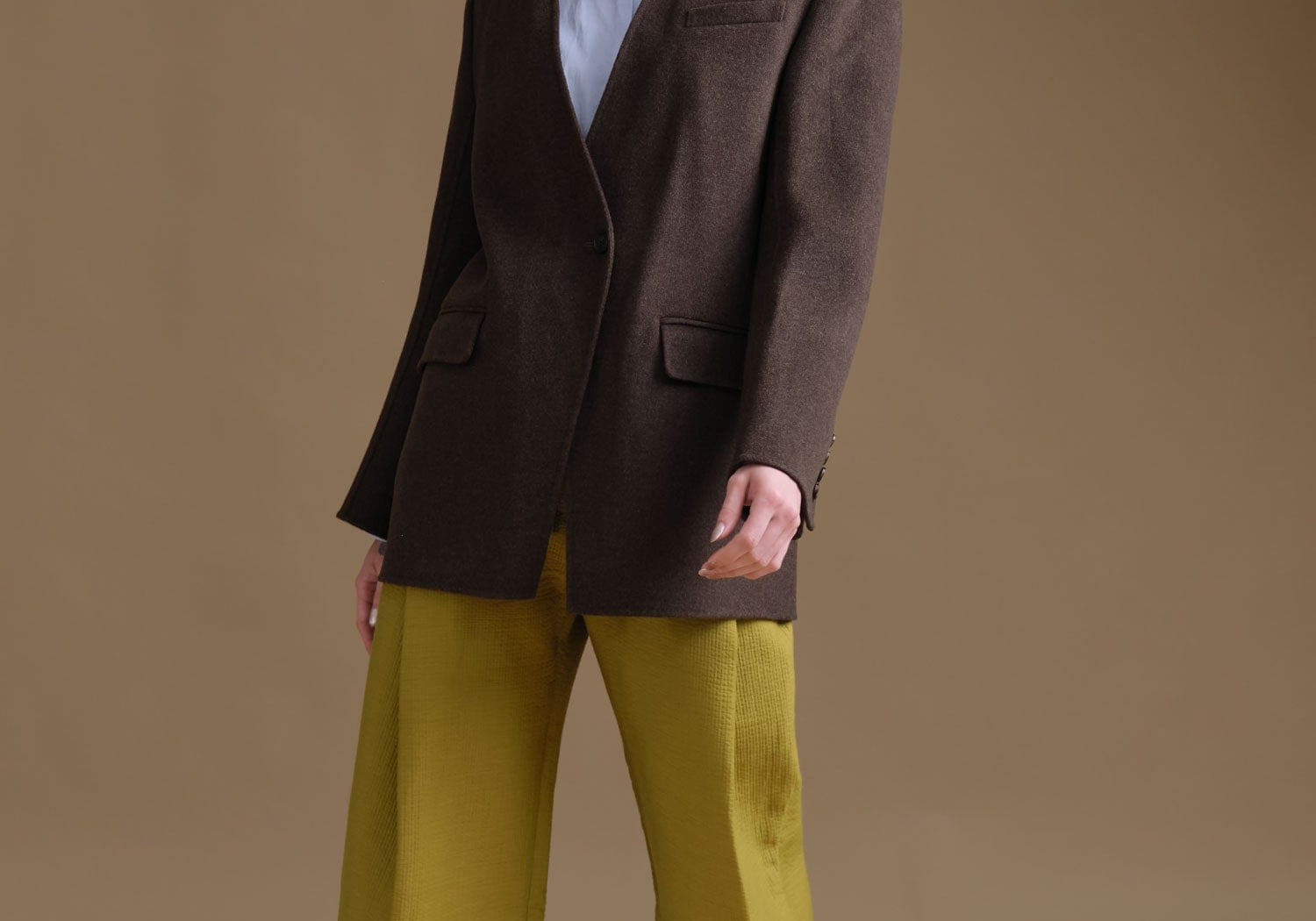 Person wearing a brown Rachel Comey blazer and green pants against a beige background