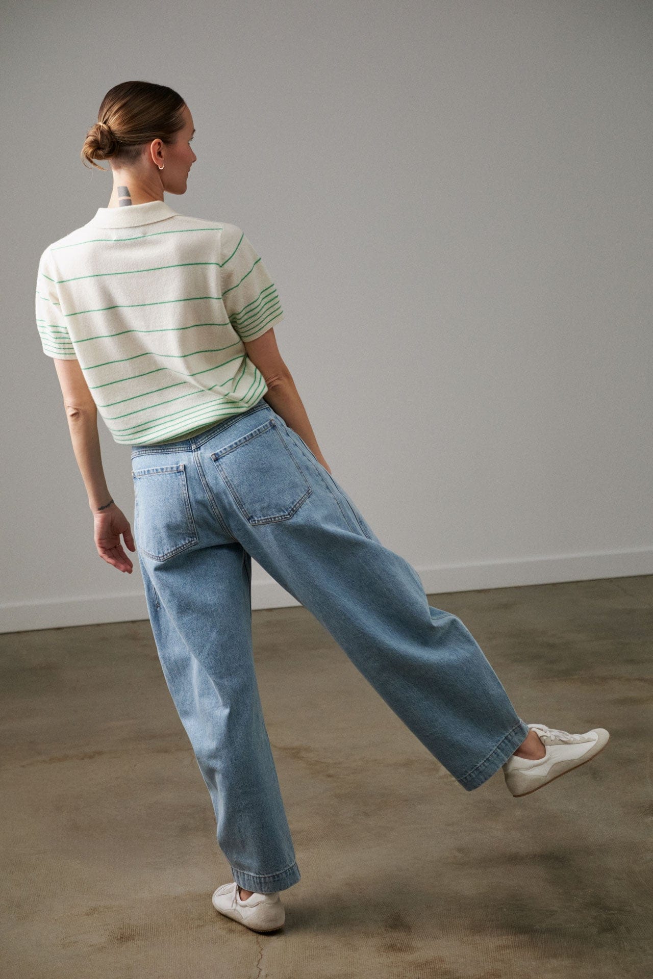 Person wearing a Demylee Cashmere striped polo shirt and Rachel Comey blue jeans standing against a plain wall.