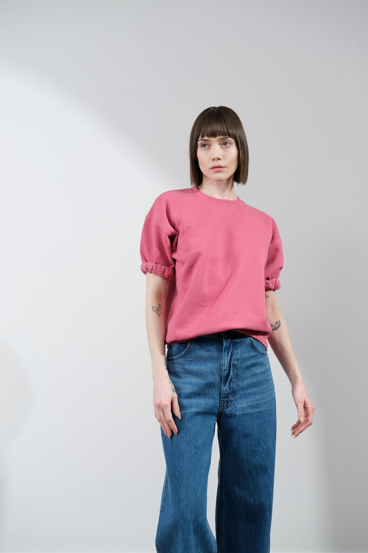 Person wearing a pink Rachel Comey stanz sweatshirt and blue jeans against a plain background