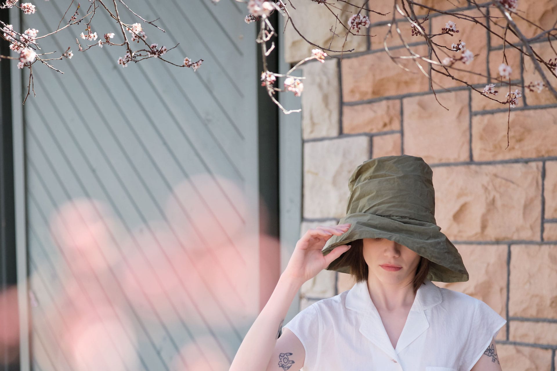 Person wearing a travel hat from Reinhard Plank outdoors with cherry blossom branches in the foreground.