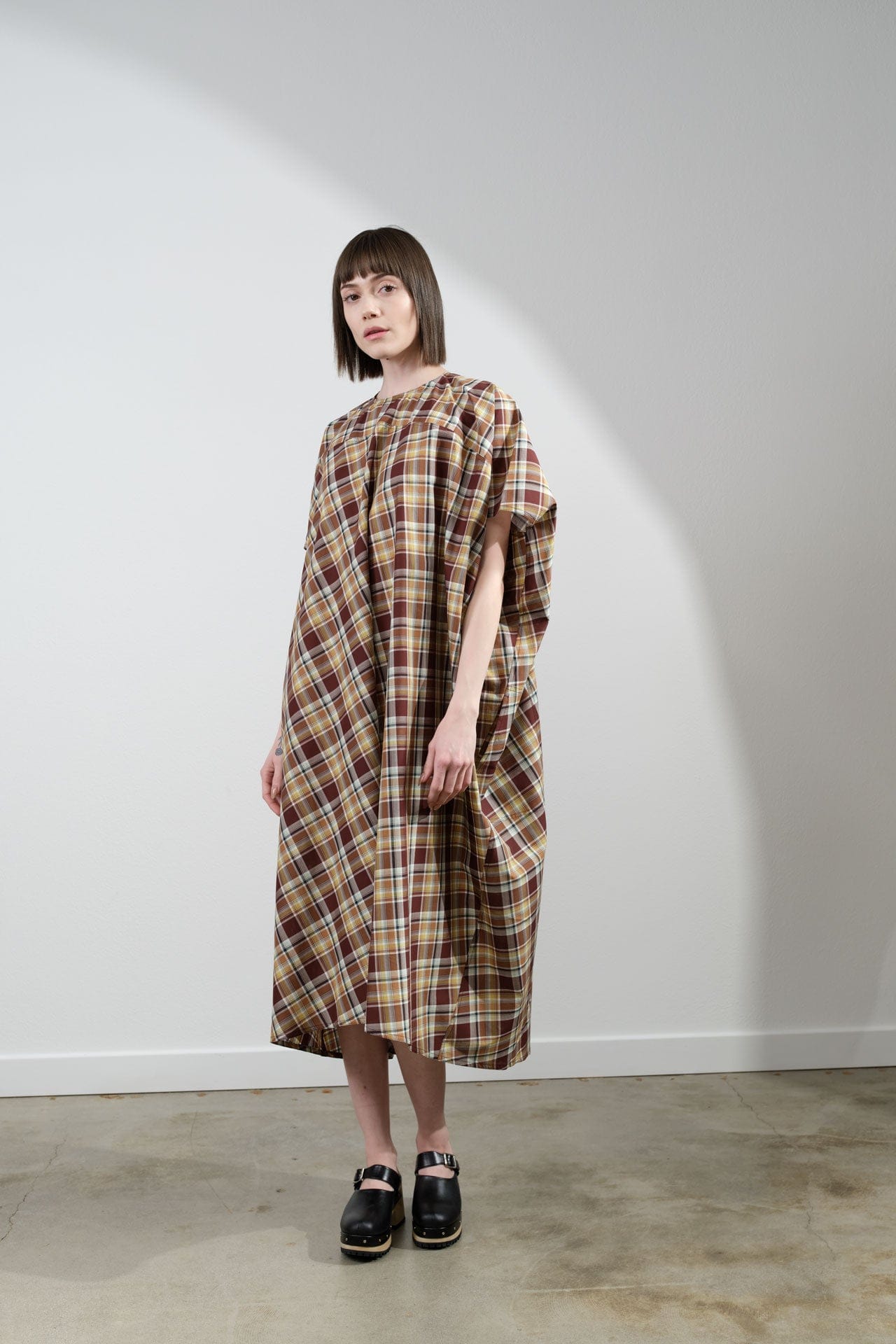 Woman wearing a Sofie D'Hoore plaid dress standing against a white wall.