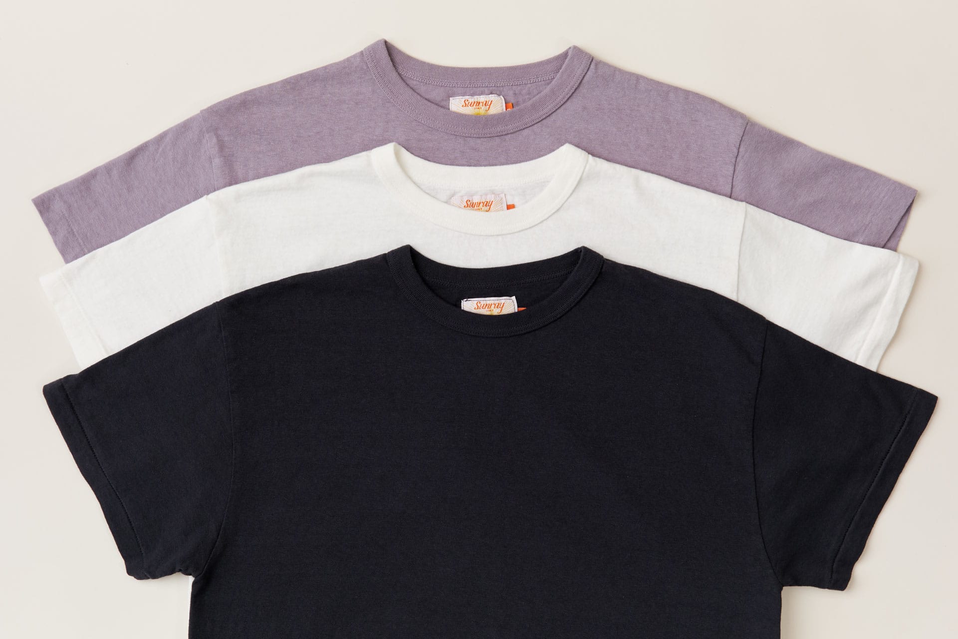Three Sunray Sportwear t-shirts for women in black, white, and purple on a light gray background