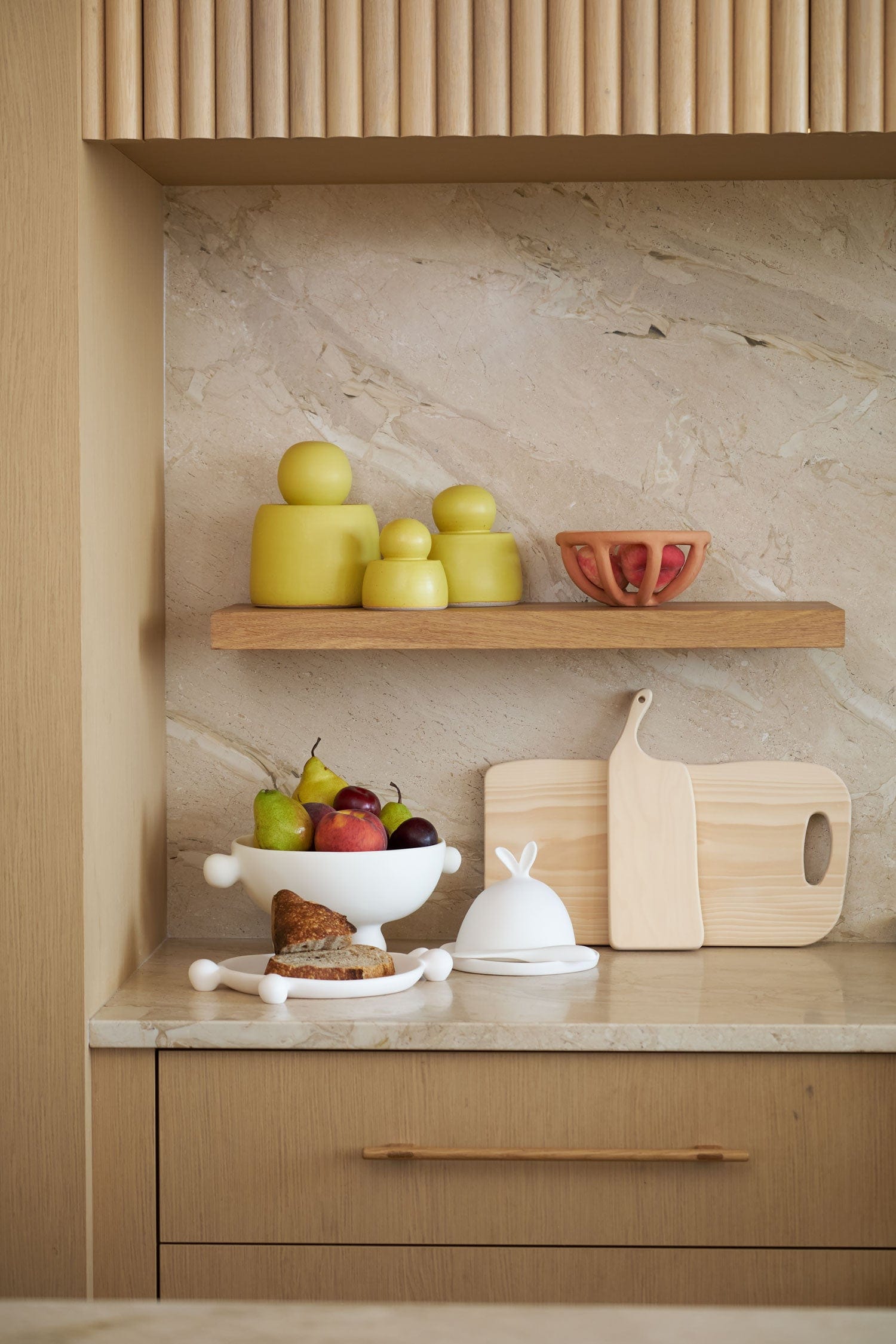 Kitchen counter with virginia sin prong fruit bowls, mh ceramic canisters and woodpecker cutting boards against a stone wall.